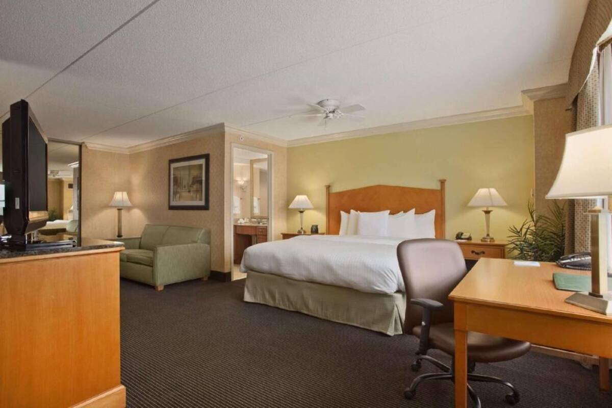 Una habitación de hotel con cama, escritorio, silla, televisor y ventilador de techo.