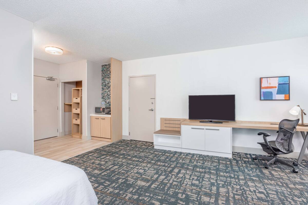 Hotellihuone, jossa on sänky, työpöytä tietokoneella, tuoli, televisio ja vaatekaappi.