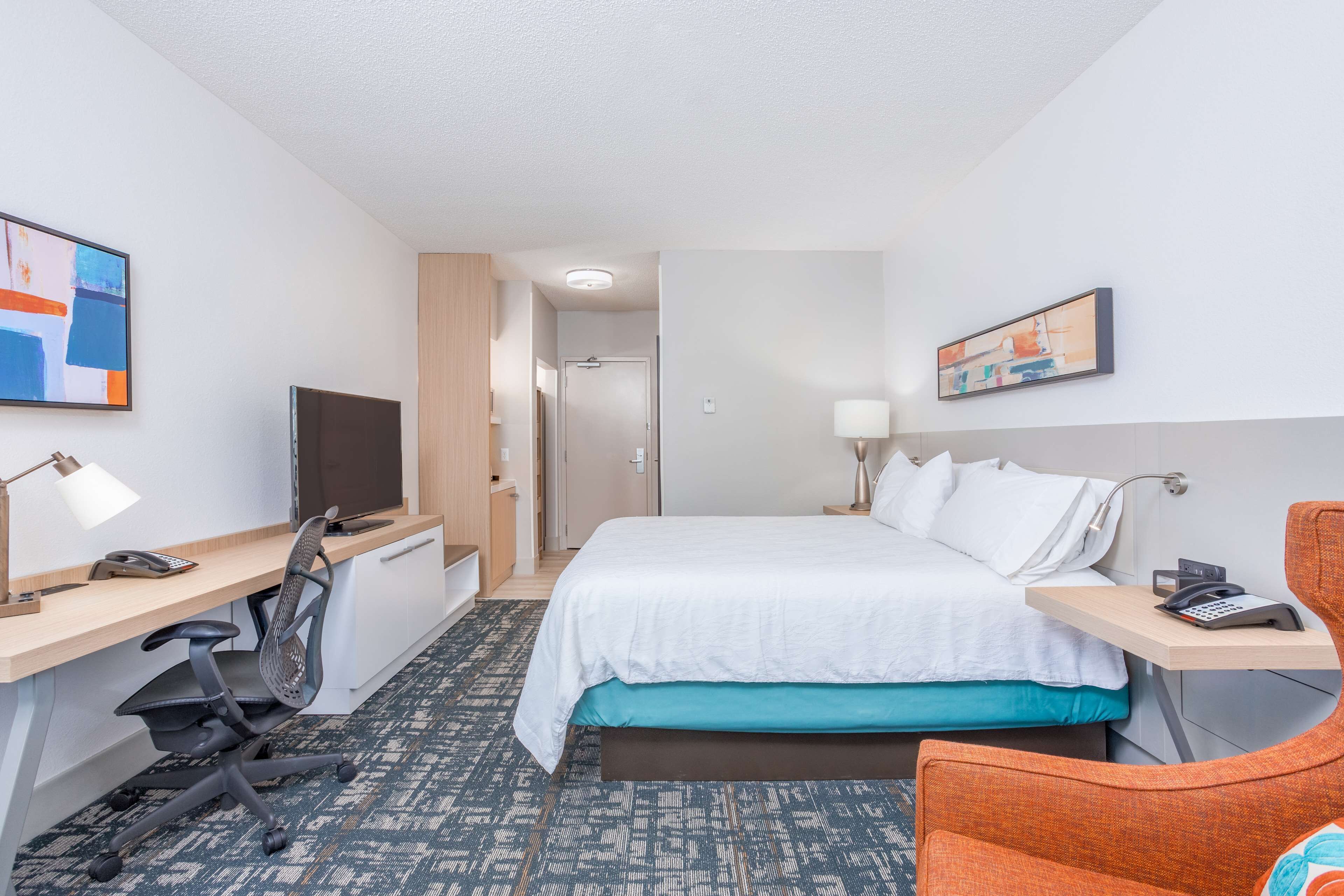 Ein Hotelzimmer mit Bett, Schreibtisch, Stuhl, Fernseher und Bildern an den Wänden.