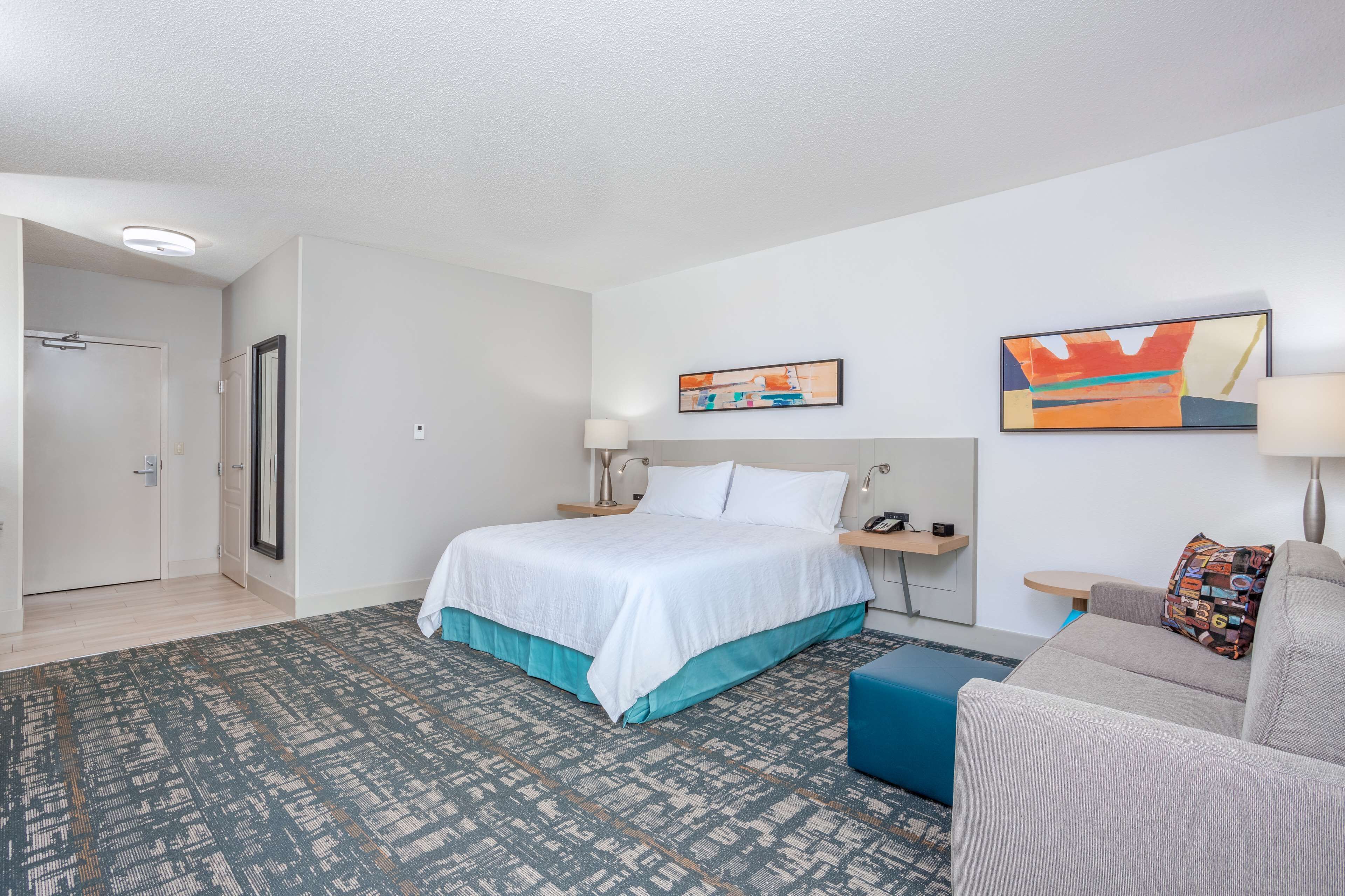 A hotel room with a bed, a sofa, a desk, and two paintings on the wall.