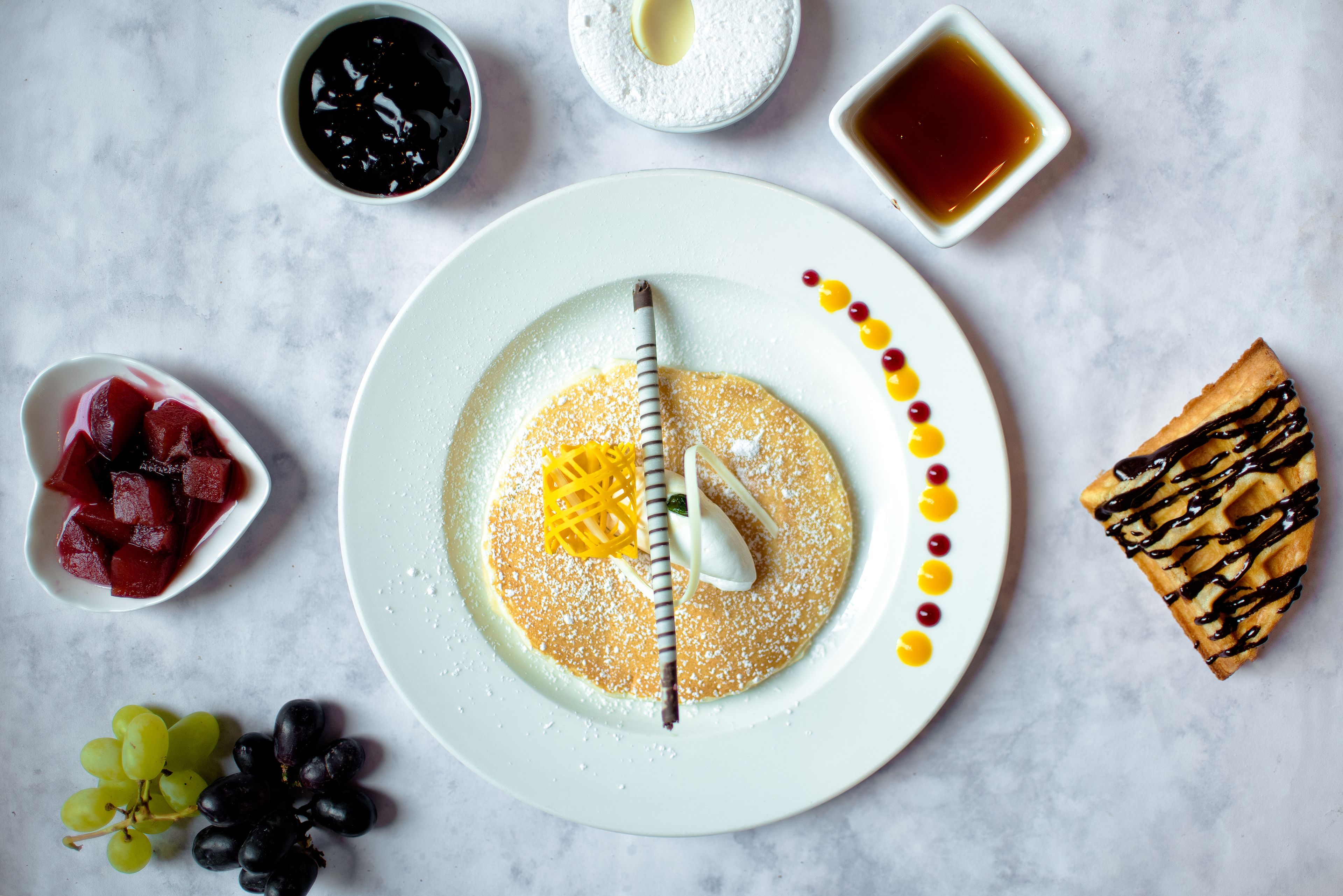 A plate with a dessert, surrounded by bowls of fruit and condiments.