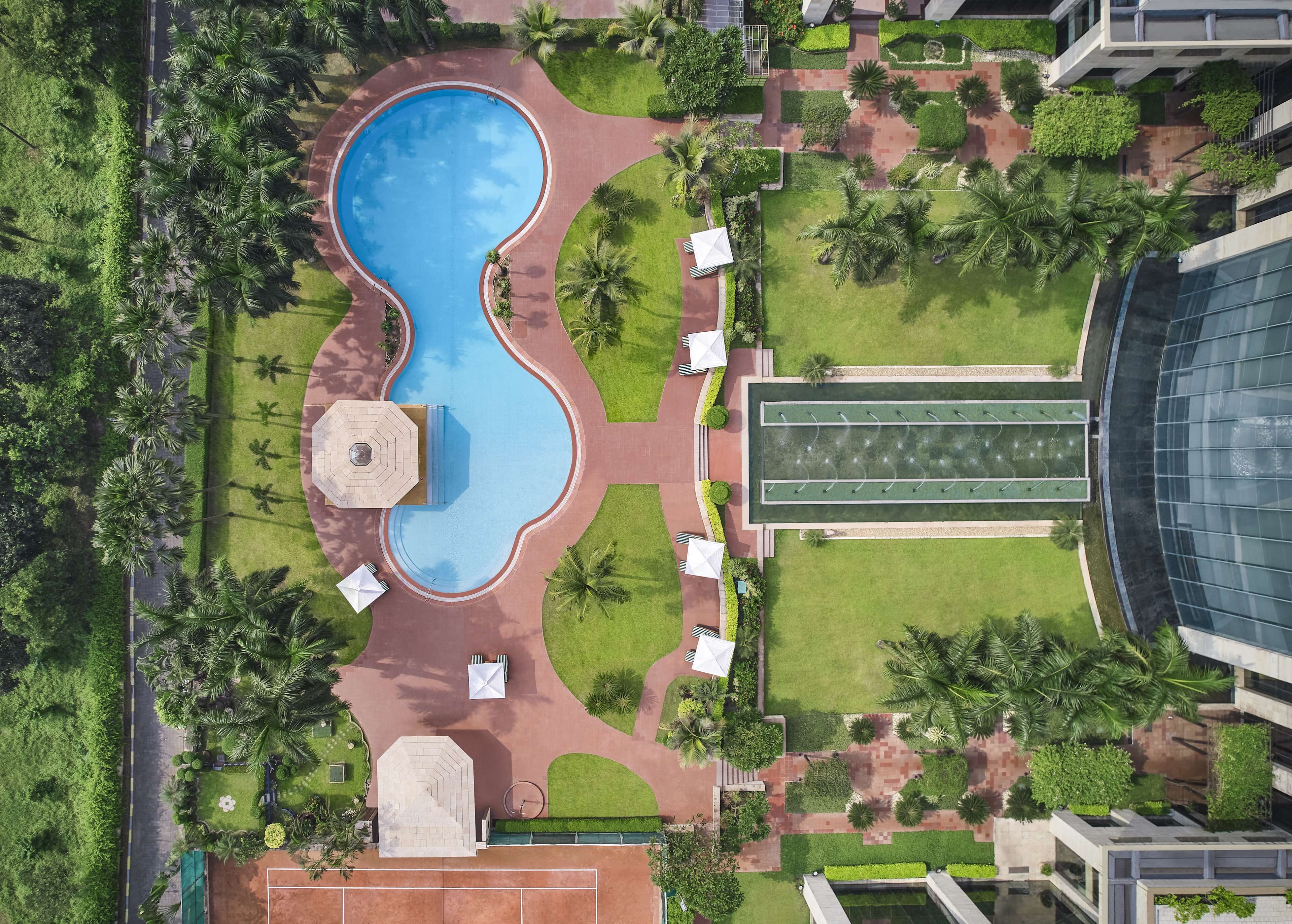 An aerial view of a resort with a central swimming pool, a tennis court, and surrounding greenery.