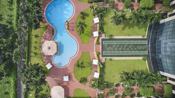 Vista aérea de un complejo turístico con una piscina central, cancha de tenis y follaje circundante.