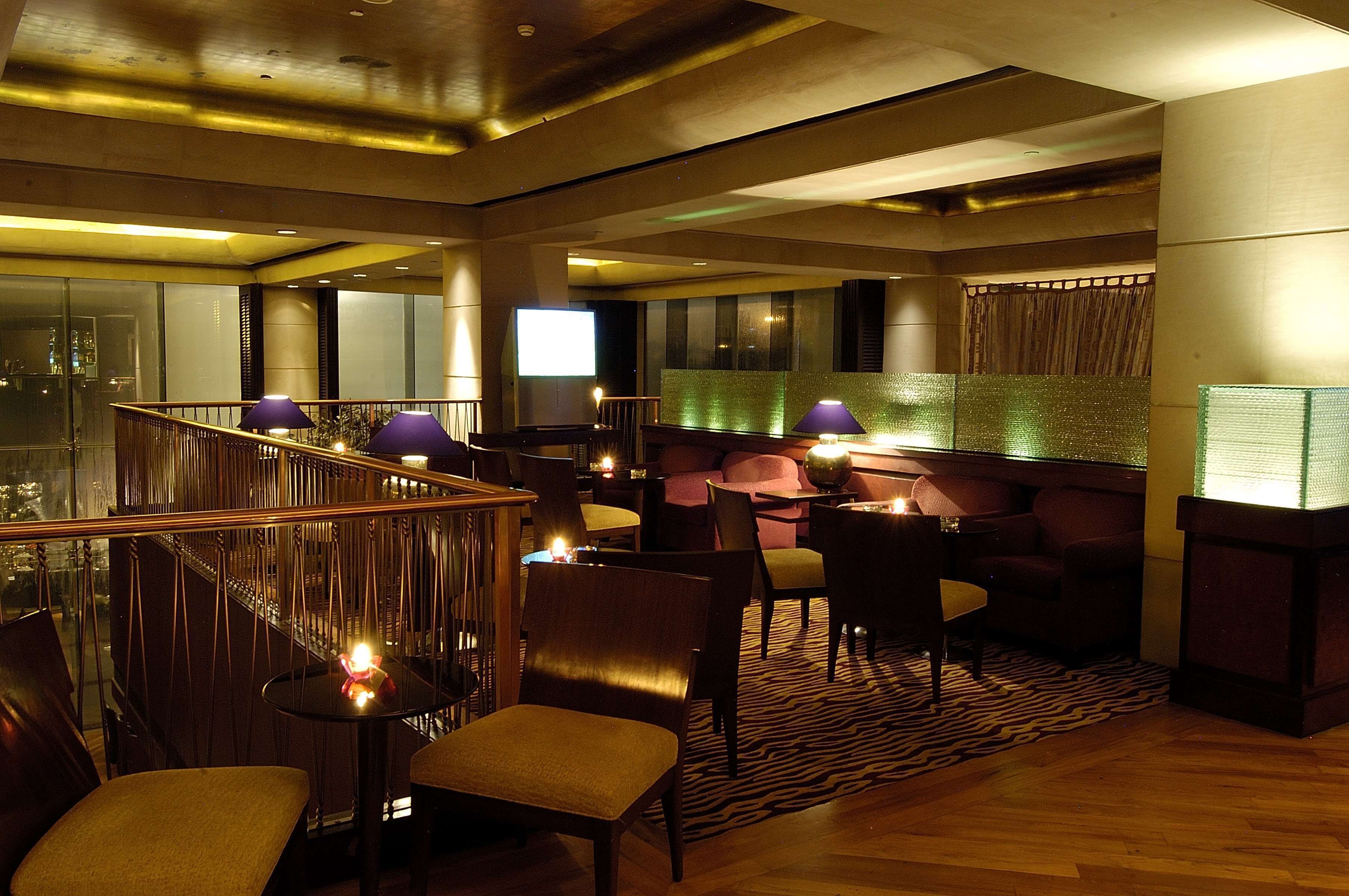 A modern lounge area with a high ceiling, a wooden staircase, and a seating arrangement including chairs and sofas.