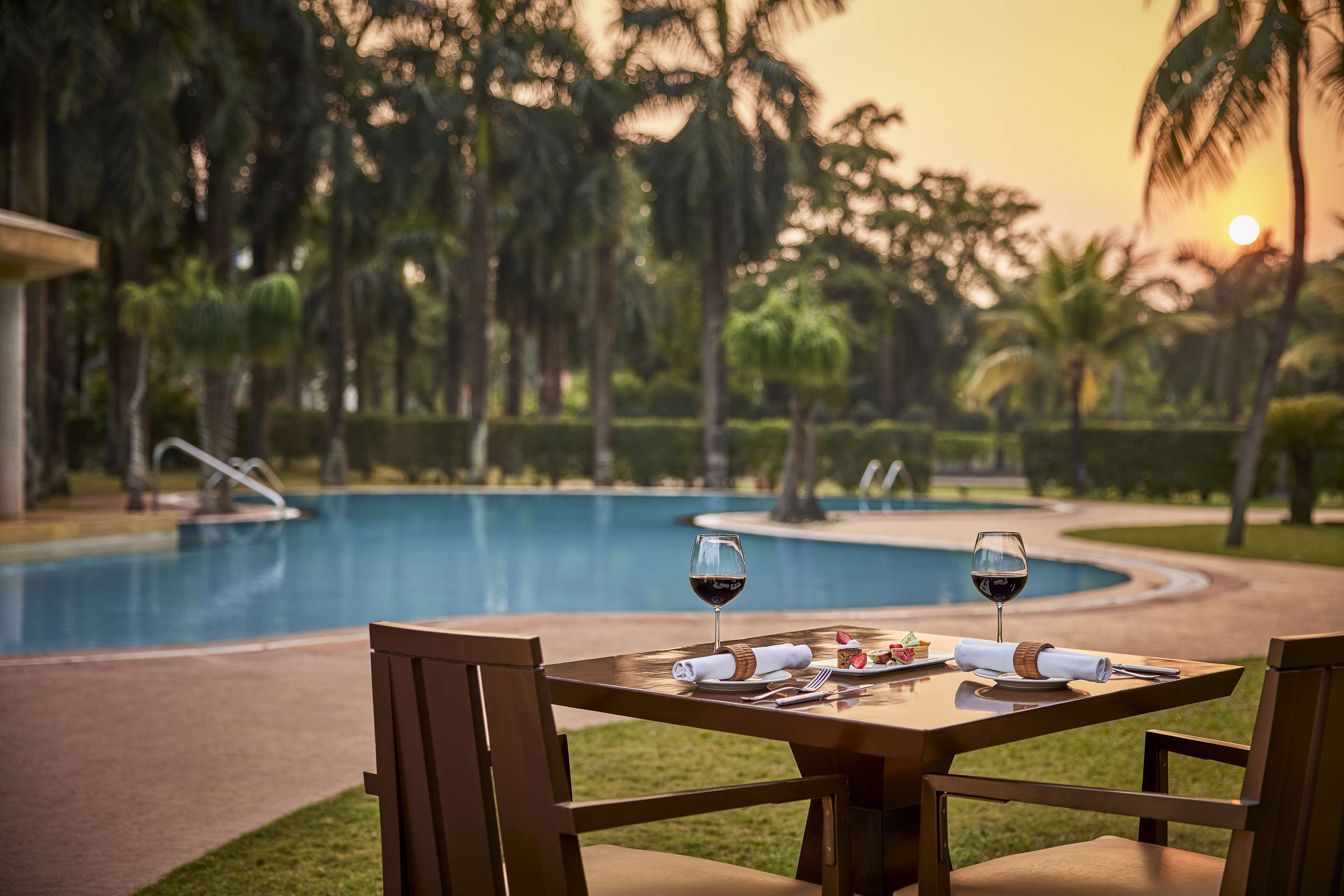Mesa para dos con vista a una piscina y palmeras al atardecer.