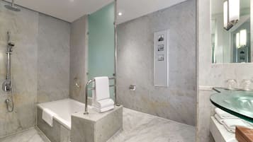 A modern bathroom with a marble floor, a glass sink, a bathtub, and a shower.