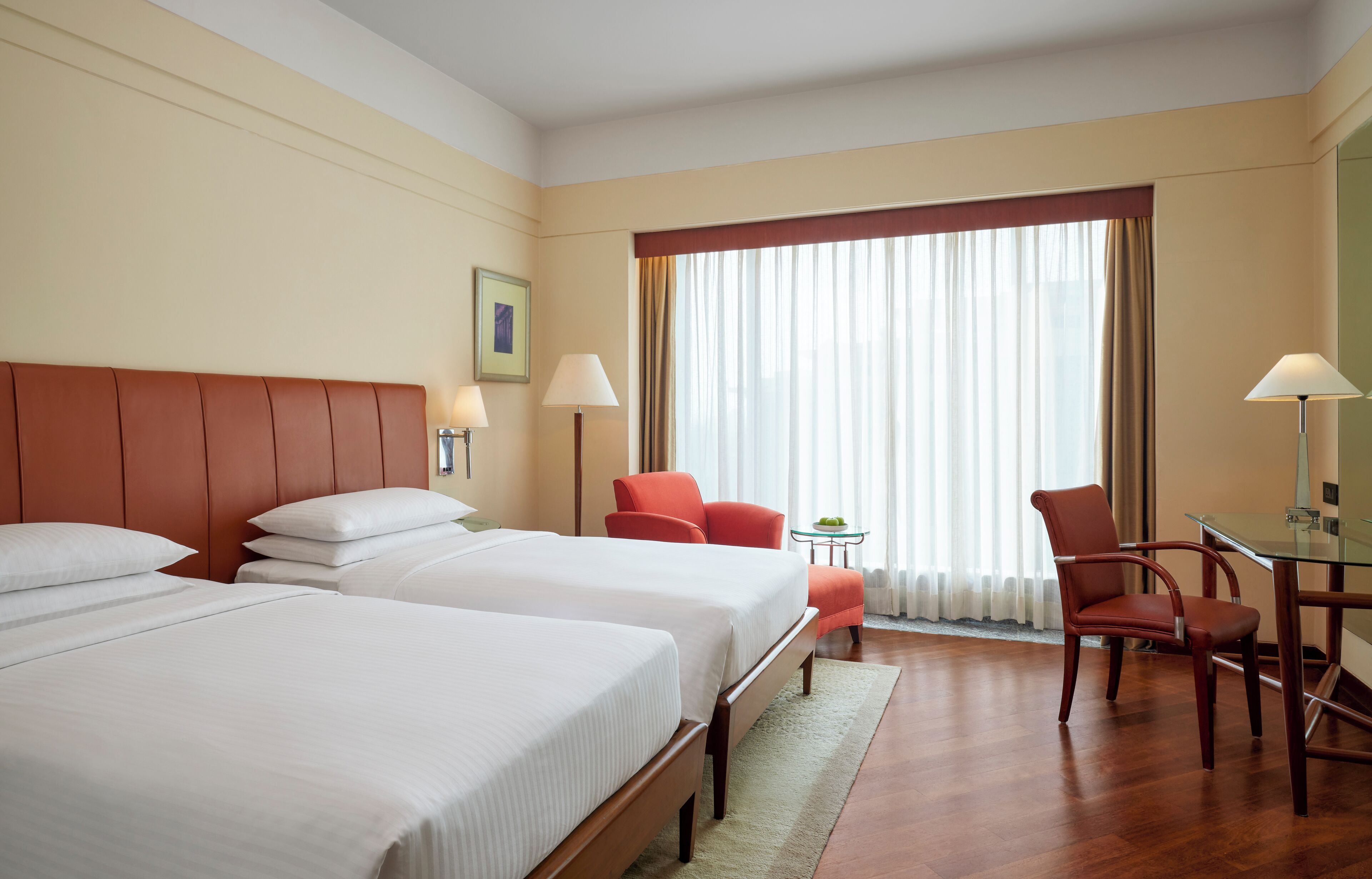 A hotel room with two beds, a desk, a chair, and a window with curtains.