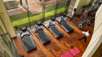 Ein Fitnessstudio mit Laufbändern, Crosstrainern und einer pinken Yogamatte.
