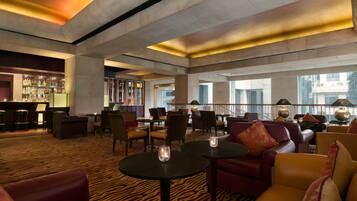 A spacious lobby with leather seating, a bar area, and large windows offering views of the city.