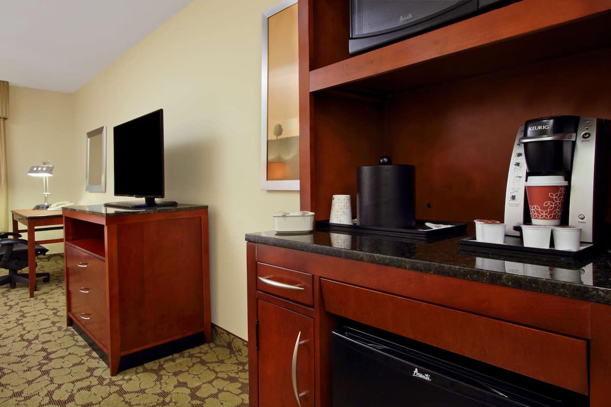 A hotel room with a wooden desk, a flat-screen TV, a coffee maker, and a microwave.