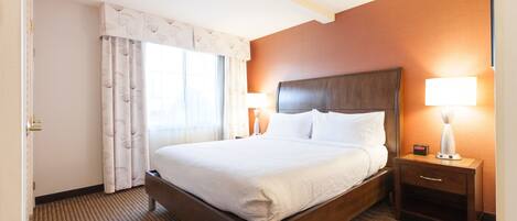 A hotel room with a large bed, two bedside tables with lamps, a window with curtains, and a carpeted floor.