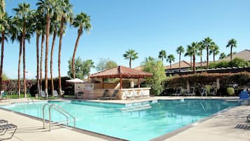 A swimming pool with lounge chairs, a small gazebo, and tall palm trees.