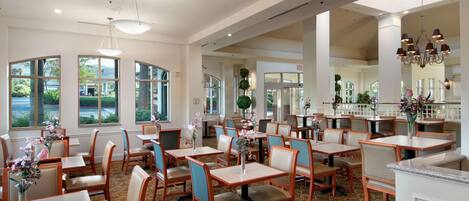 Un restaurante espacioso con techos altos, ventanas amplias y diversas opciones de asientos, incluyendo mesas y sillas.