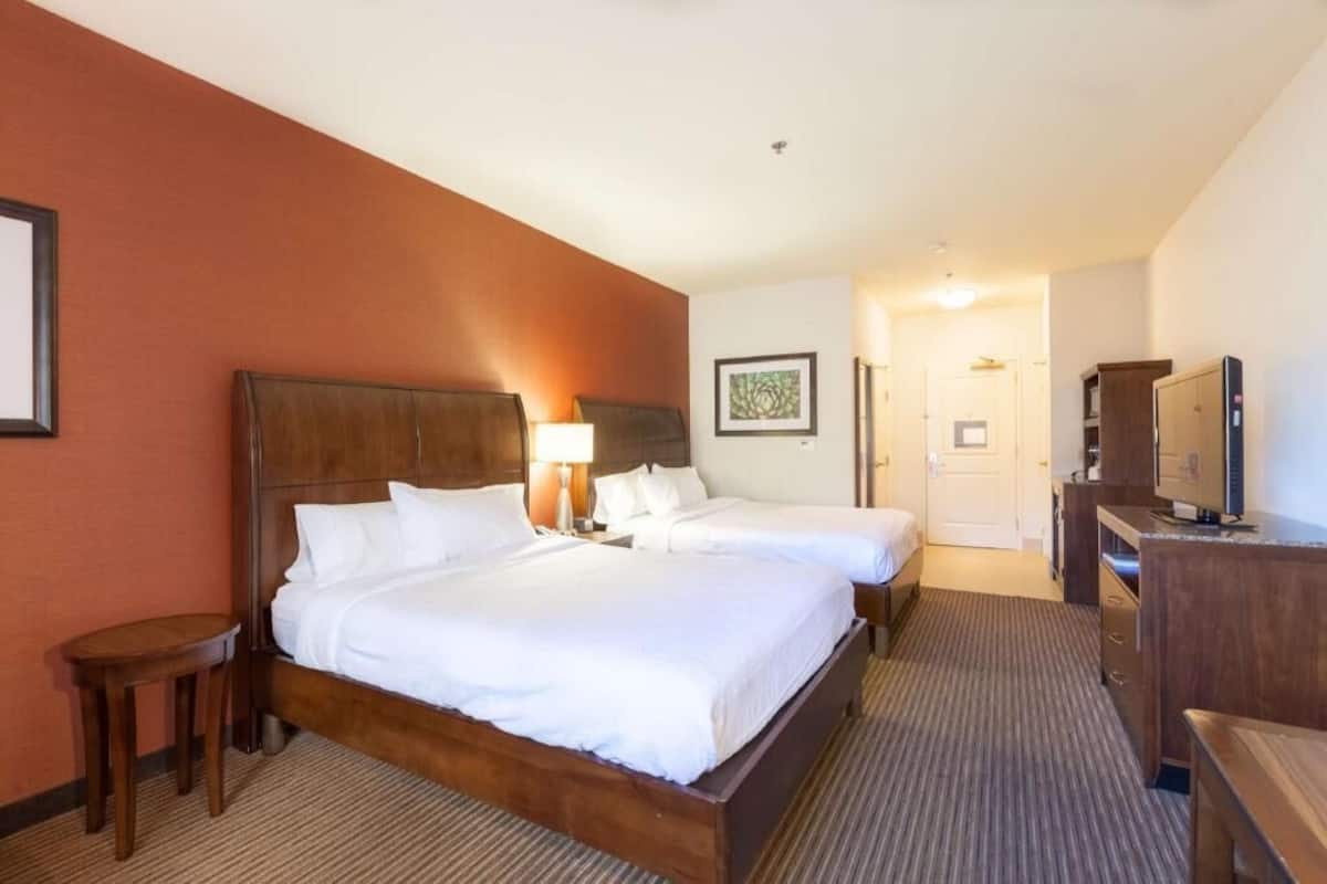 A hotel room with two beds, a desk, a chair, a TV, and a framed picture on the wall.