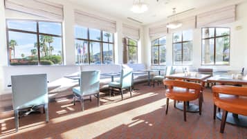 A hotel room with large windows, a patterned carpet, and a mix of modern and classic furniture.