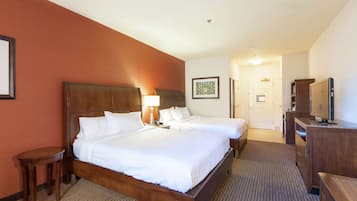 A hotel room with two beds, a desk, a chair, a TV, and a framed picture on the wall.