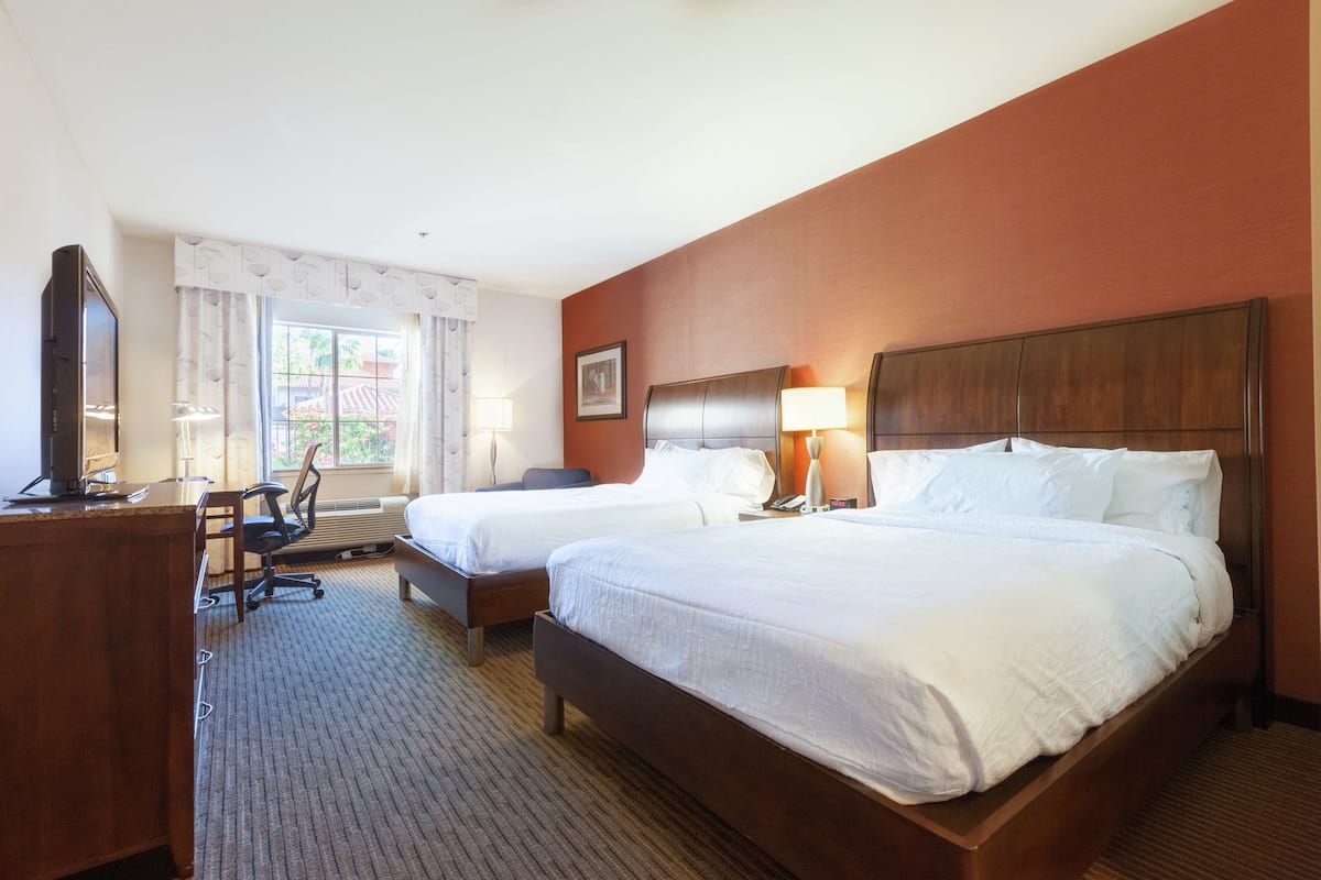 A hotel room with two beds, a desk, a chair, and a television.