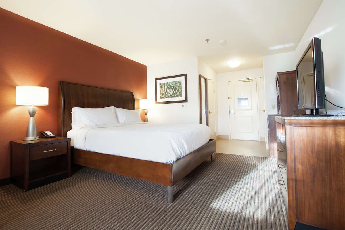 A hotel room with a bed, bedside lamps, a desk with a phone, a television, and a framed picture on the wall.