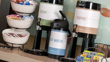 A coffee station with decaf, coffee, and hot water dispensers, and a bowl of snacks.