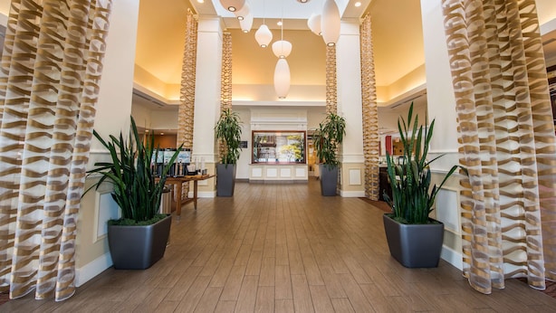 A spacious lobby with a high ceiling, large potted plants, and a central reception area.