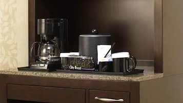 A kitchen area with a microwave, coffee maker, and a coffee mug on the countertop.