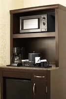 A kitchen area with a microwave, coffee maker, and a coffee mug on the countertop.