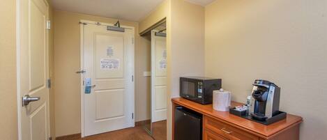 Habitación de hotel con una kitchenette compacta, que incluye microondas, cafetera y un refrigerador pequeño.