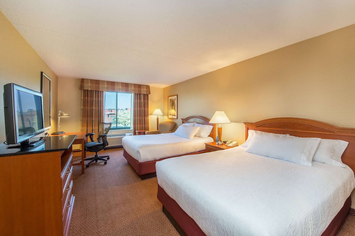A hotel room with two beds, a desk with a television, and a window with curtains.