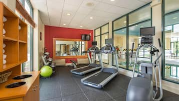 A gym with treadmills, an elliptical, and a ball. There are windows and a mirror.