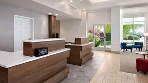 Un hall d'accueil moderne avec un comptoir en bois, une enseigne indiquant « Hilton Honors » et une vue sur l’extérieur grâce à de grandes fenêtres.