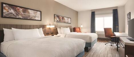 A hotel room with two beds, a desk, a chair, and artwork on the walls.