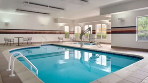 Une piscine avec une terrasse carrelée, un transat et une petite table avec des chaises.
