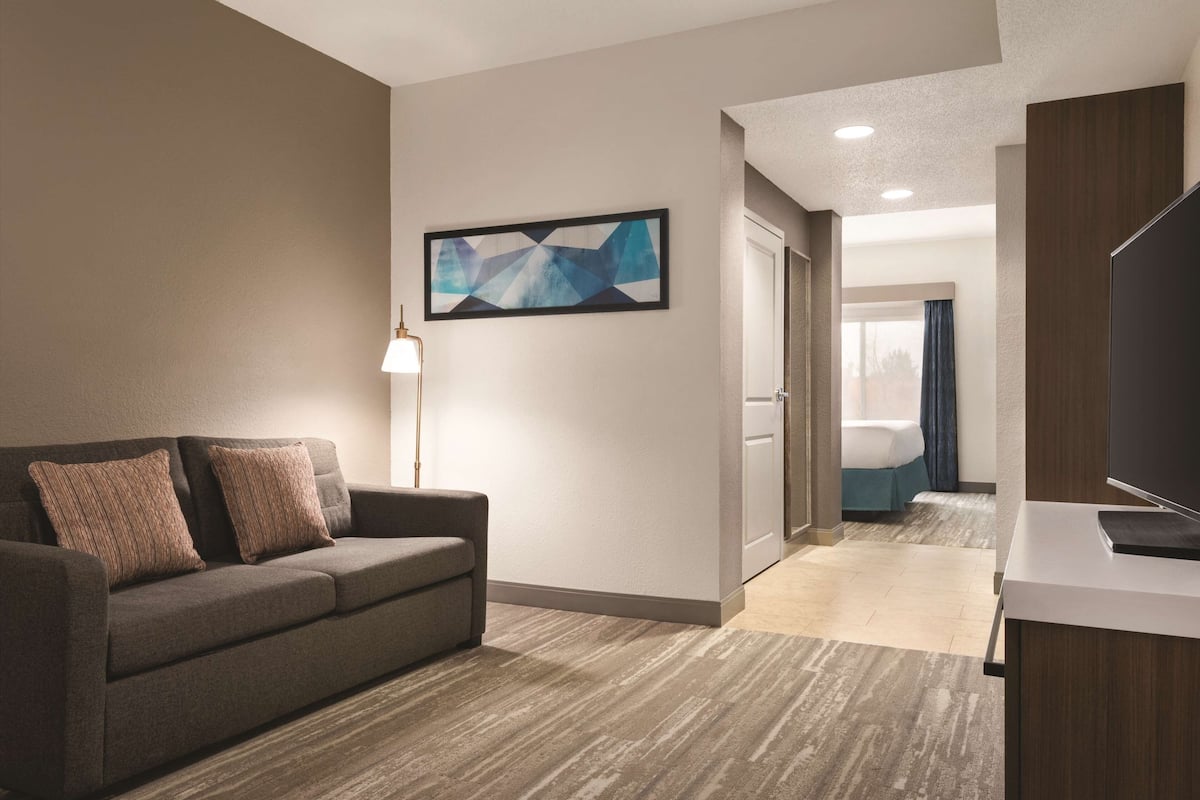 A hotel room with a sofa, a lamp, a flat-screen TV, and a painting on the wall.