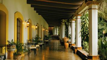 Stunning corridor with columns, tables, and chairs, surrounded by lush greenery and a staircase leading to the upper level.