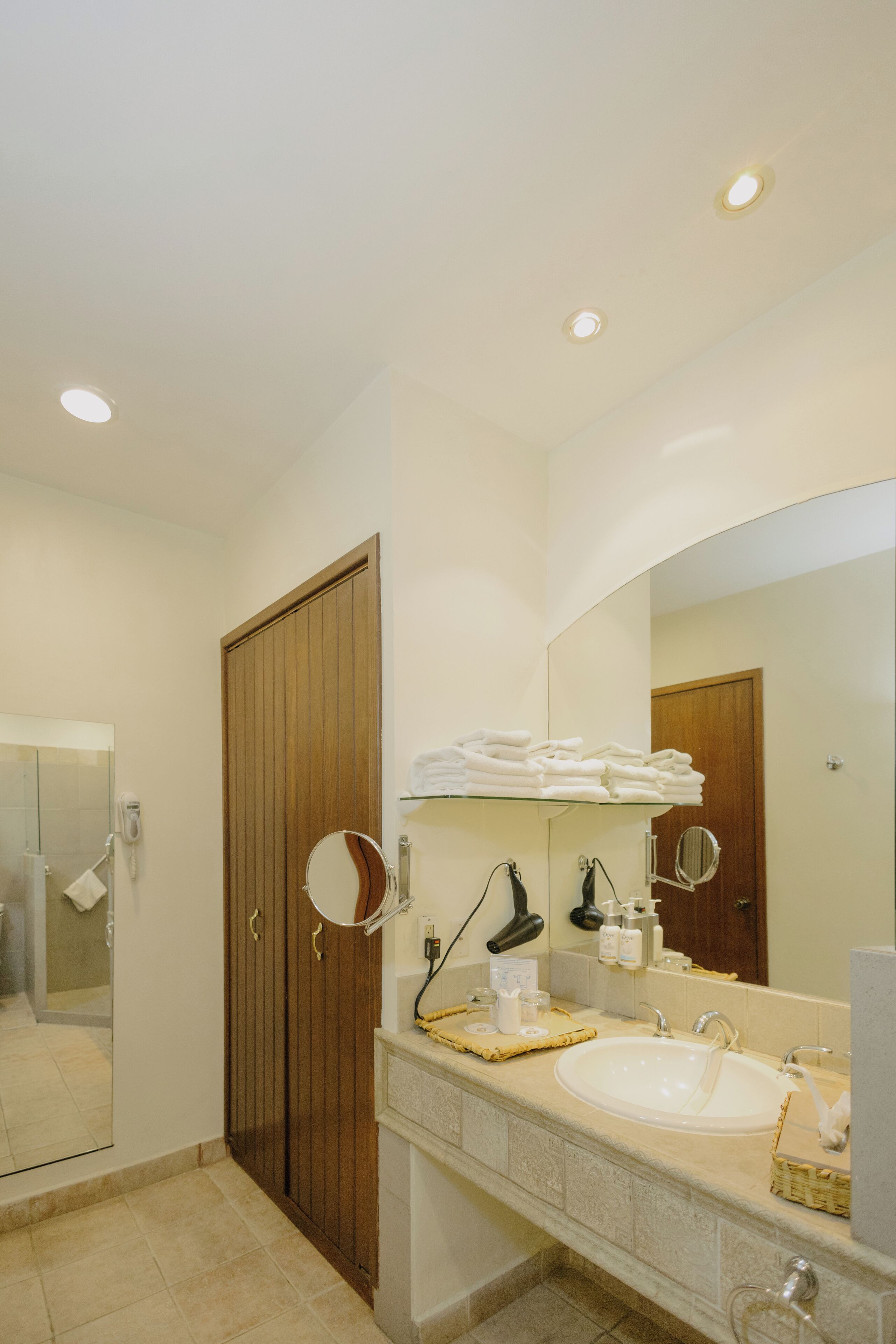 A bathroom with a wooden door, a large mirror, a sink, and a towel rack.