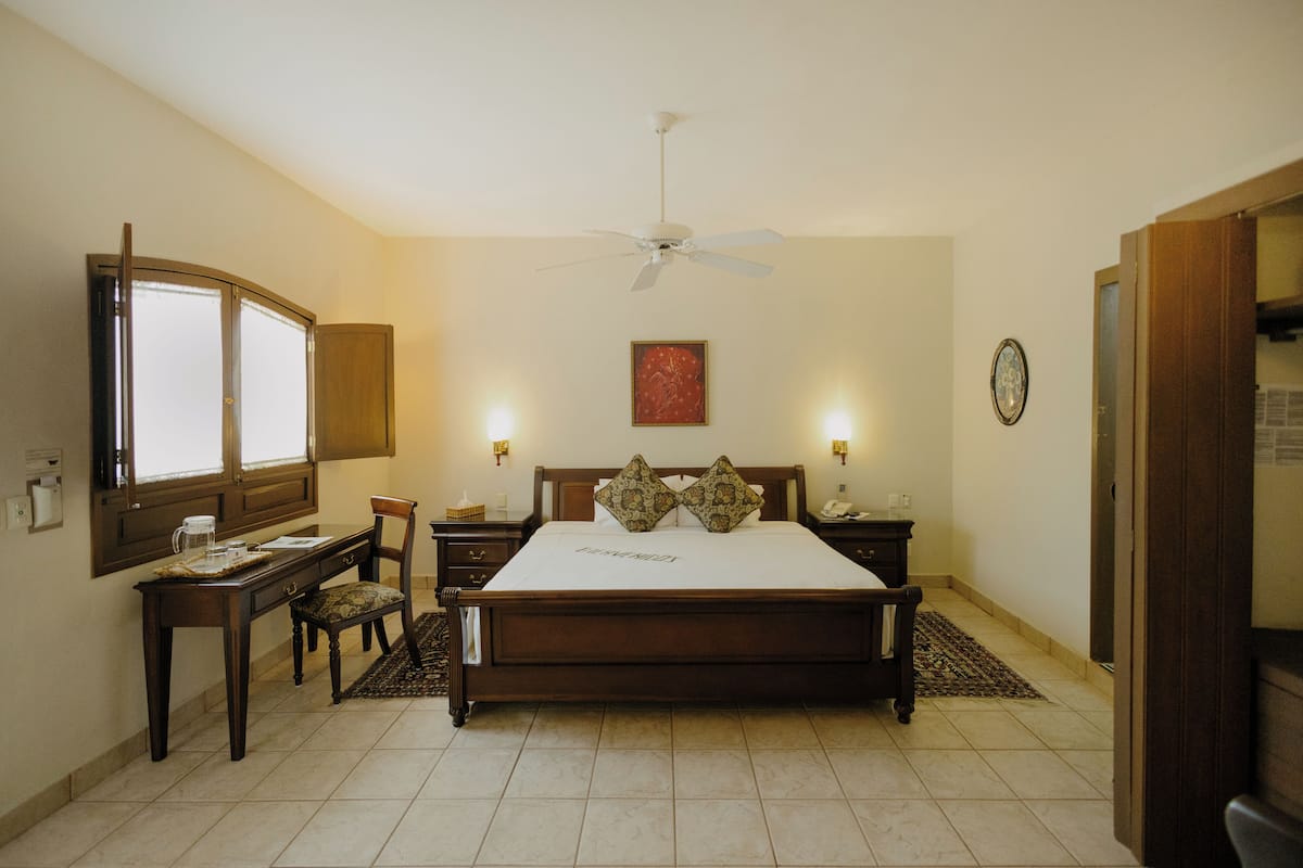 Quarto com uma cama grande, uma escrivaninha com cadeira, mesa de cabeceira e ventilador de teto.
