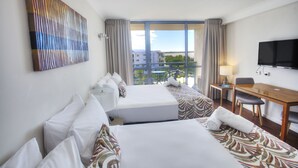 Habitación de hotel con dos camas, un escritorio, un televisor y un ventanal con vistas a la ciudad.