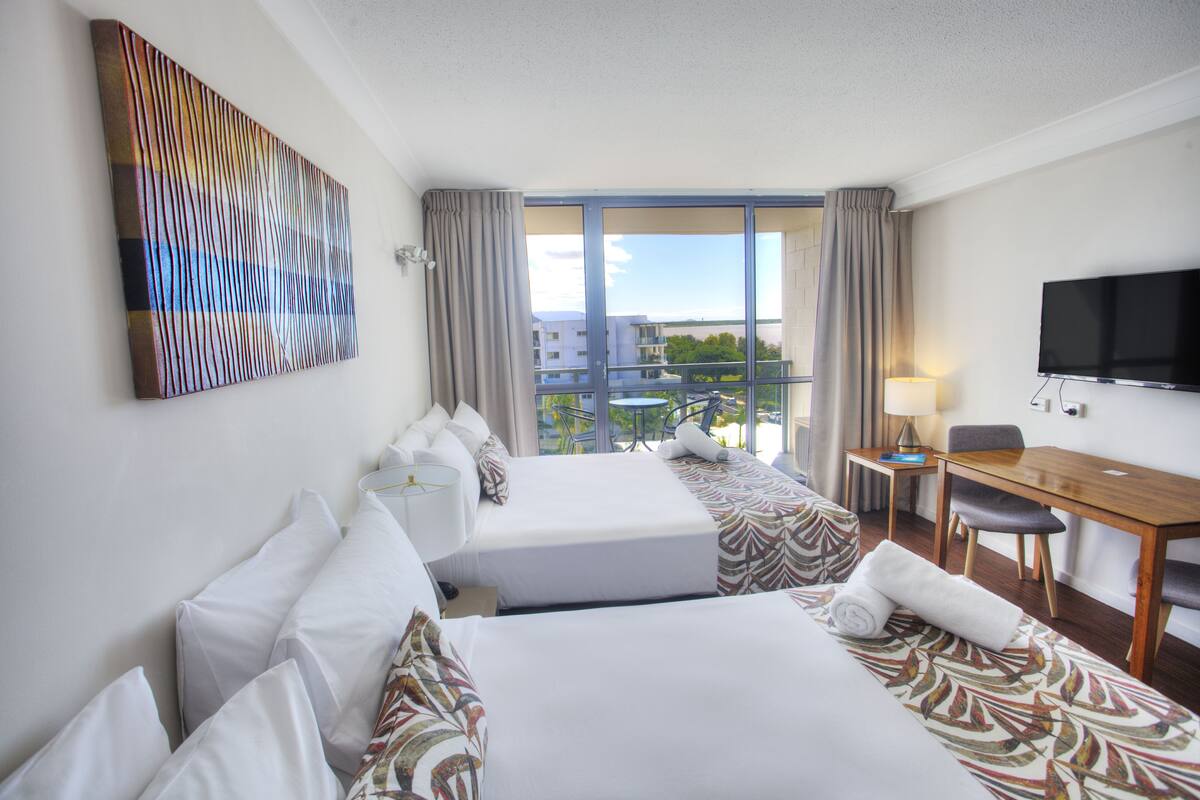 Een hotelkamer met twee bedden, een bureau, een televisie en een groot raam met uitzicht op de stad.