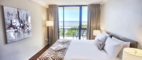 A hotel room with a large bed, a view of the sea, and a painting on the wall.