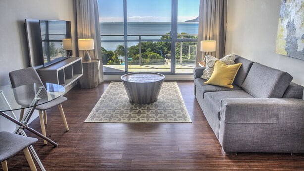 Una sala de estar moderna con un sofá, una mesa de centro de vidrio y un televisor. Cuenta con un ventanal con vista al mar.
