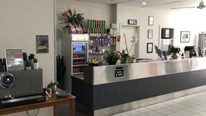 Zona de recepción con mostrador, máquina de café, refrigerador con bebidas y un cartel que indica 'Llaves y Correo'.