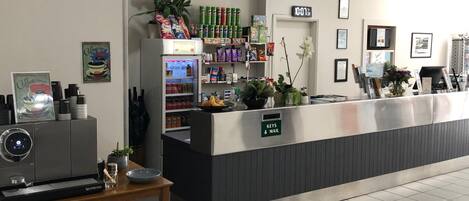 A reception area with a counter, a coffee machine, a refrigerator stocked with beverages, and a sign indicating 'Keys & Mail'.