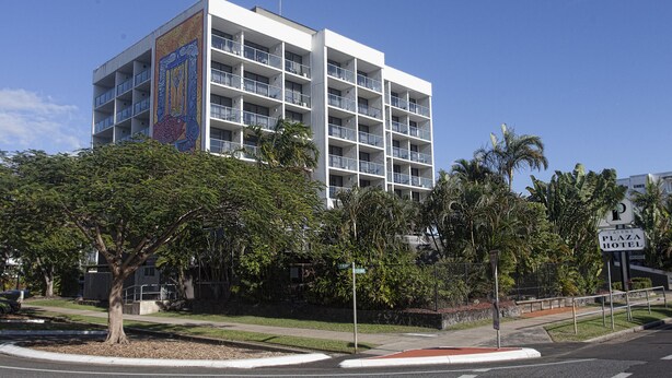 Een hotel met meerdere verdiepingen en balkons, omgeven door palmbomen en een helderblauwe lucht.