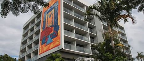 A modern hotel with multiple floors, balconies, and a large colorful mural on the side.