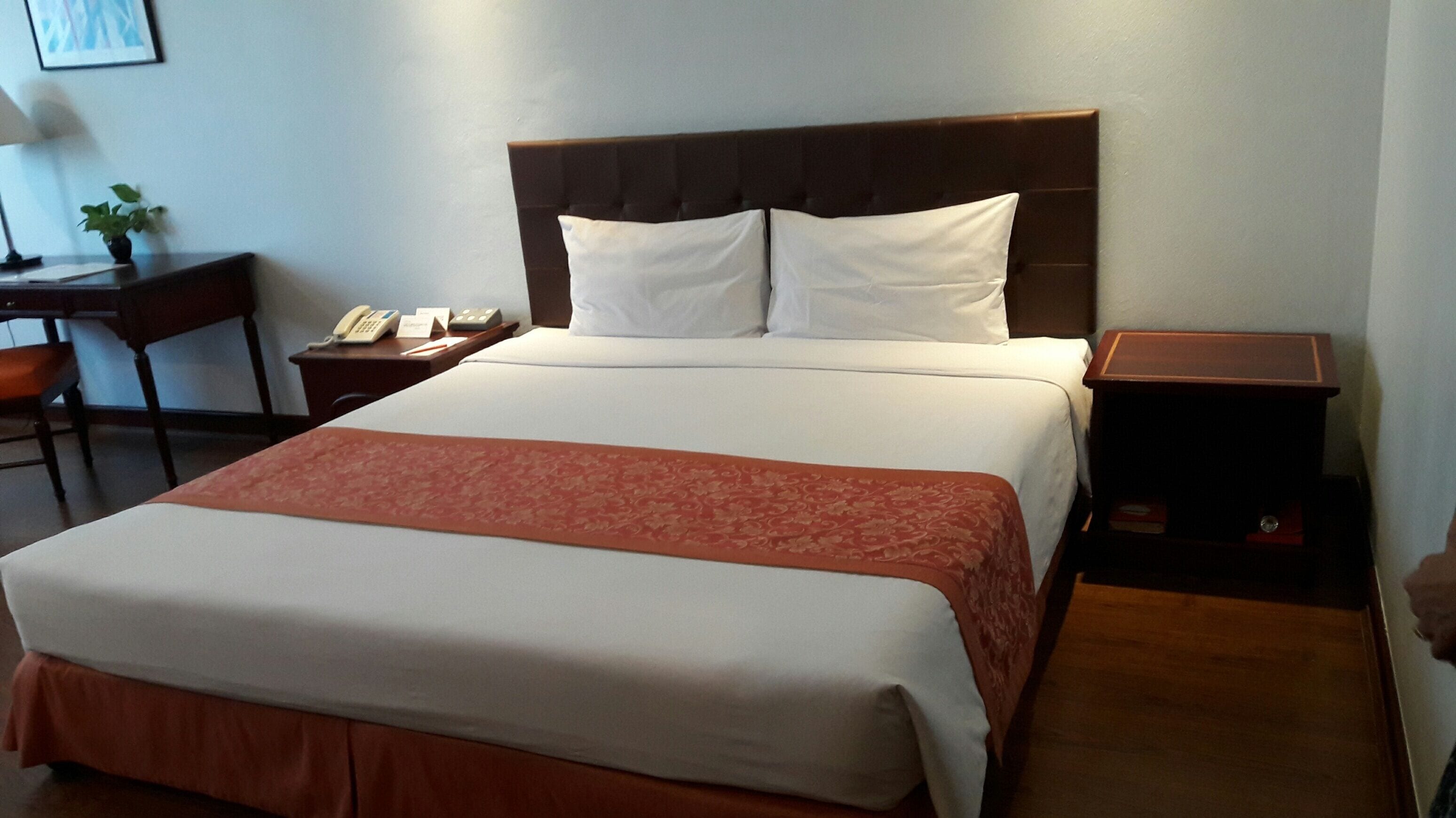 A hotel room with a large bed, a bedside table with a lamp, a small desk with a telephone, and a nightstand with a lamp.