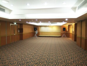 A conference room with a patterned carpet, a podium, a projector, and a speaker on a tripod. - Tai Pan Hotel (Bangkok)