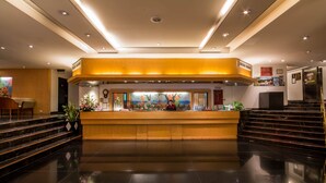A hotel reception area with a wooden reception desk, a large painting above it, and a staircase leading to an upper level. - Tai Pan Hotel (Bangkok)