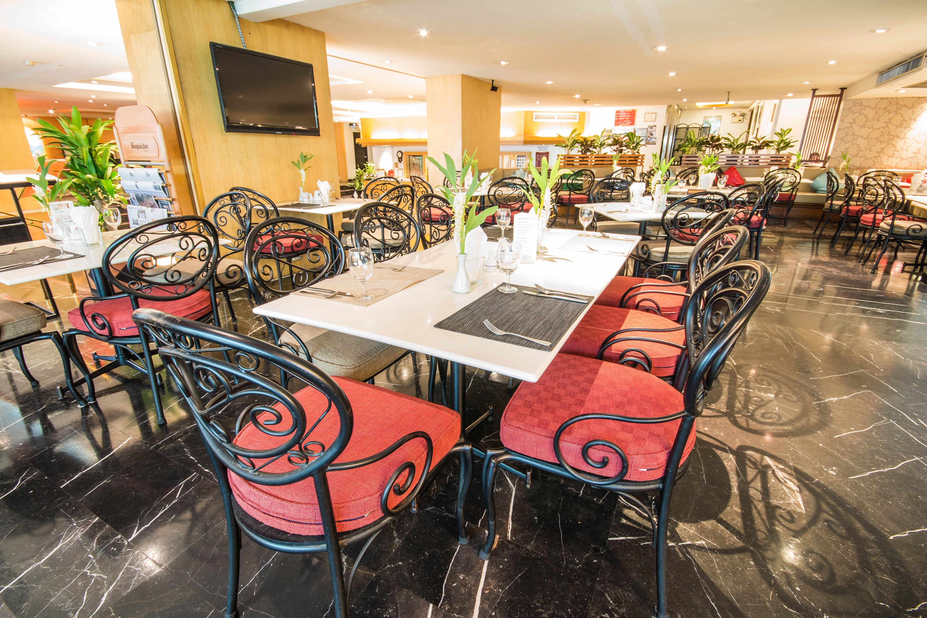 A spacious restaurant with multiple tables and chairs, featuring a modern interior with marble flooring and decorative plants.