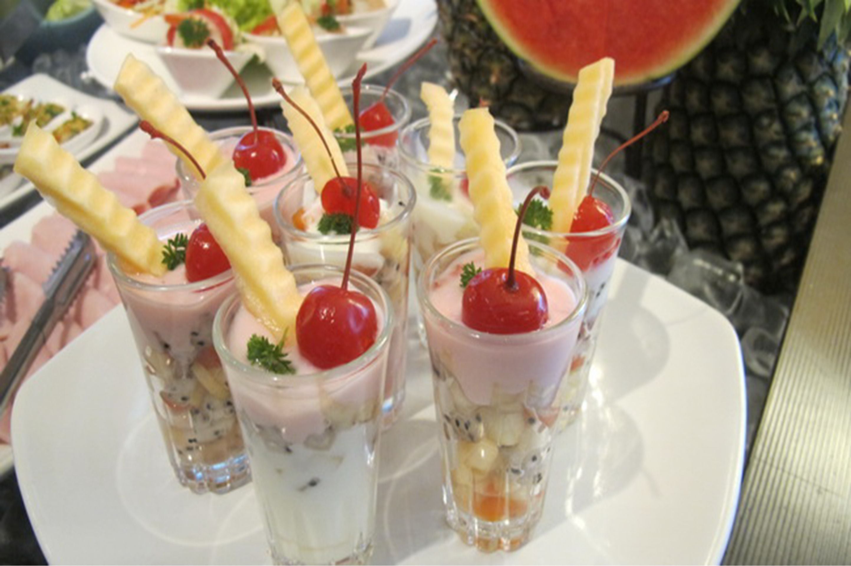Una bandeja de postres con vasos pequeños que contienen postres en capas, cerezas y palitos de oblea.