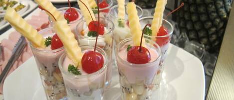 Una bandeja de postres con vasos pequeños que contienen postres en capas, cerezas y palitos de oblea.